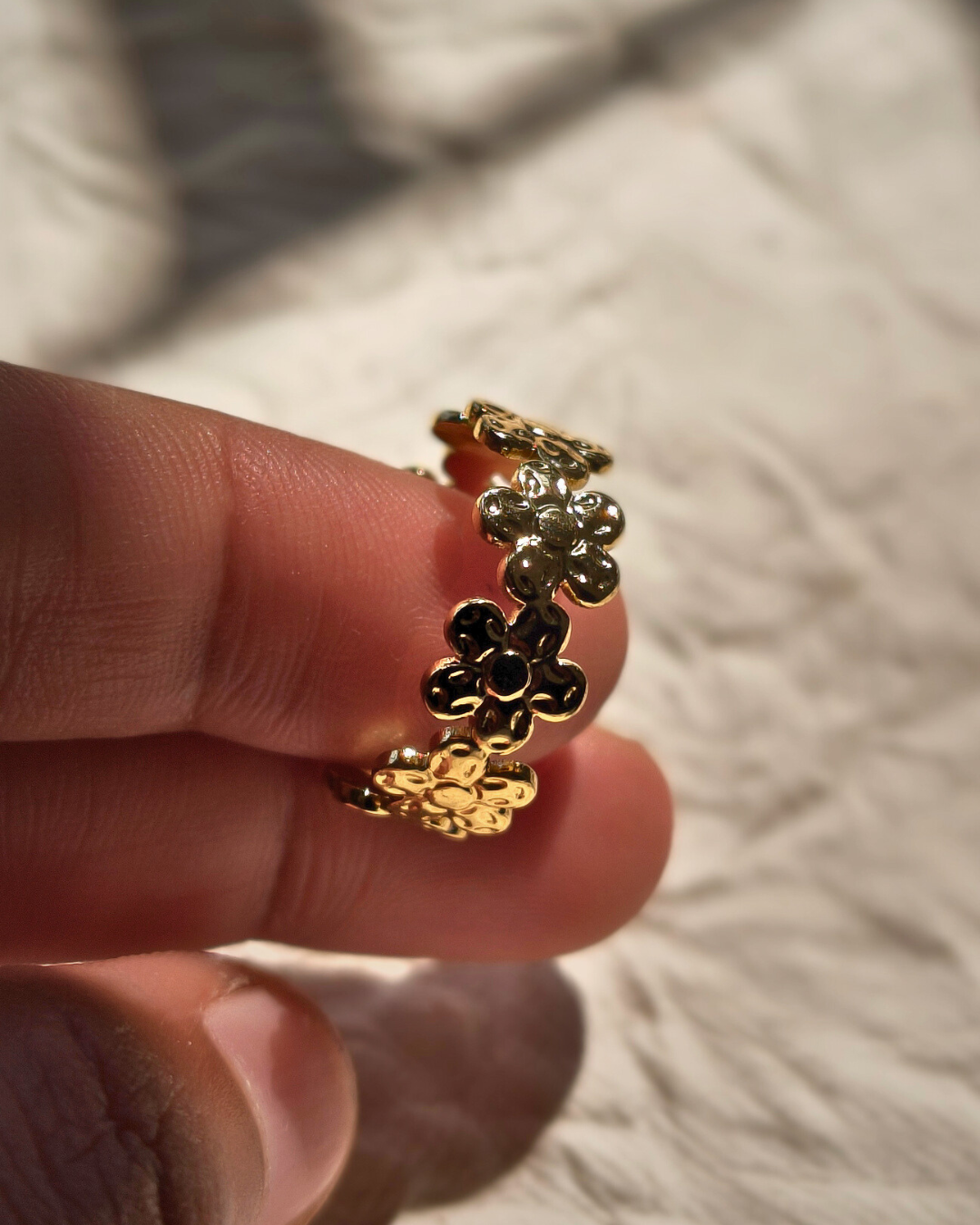 Close up of delicate flower ring with gold plating and open adjustable design.