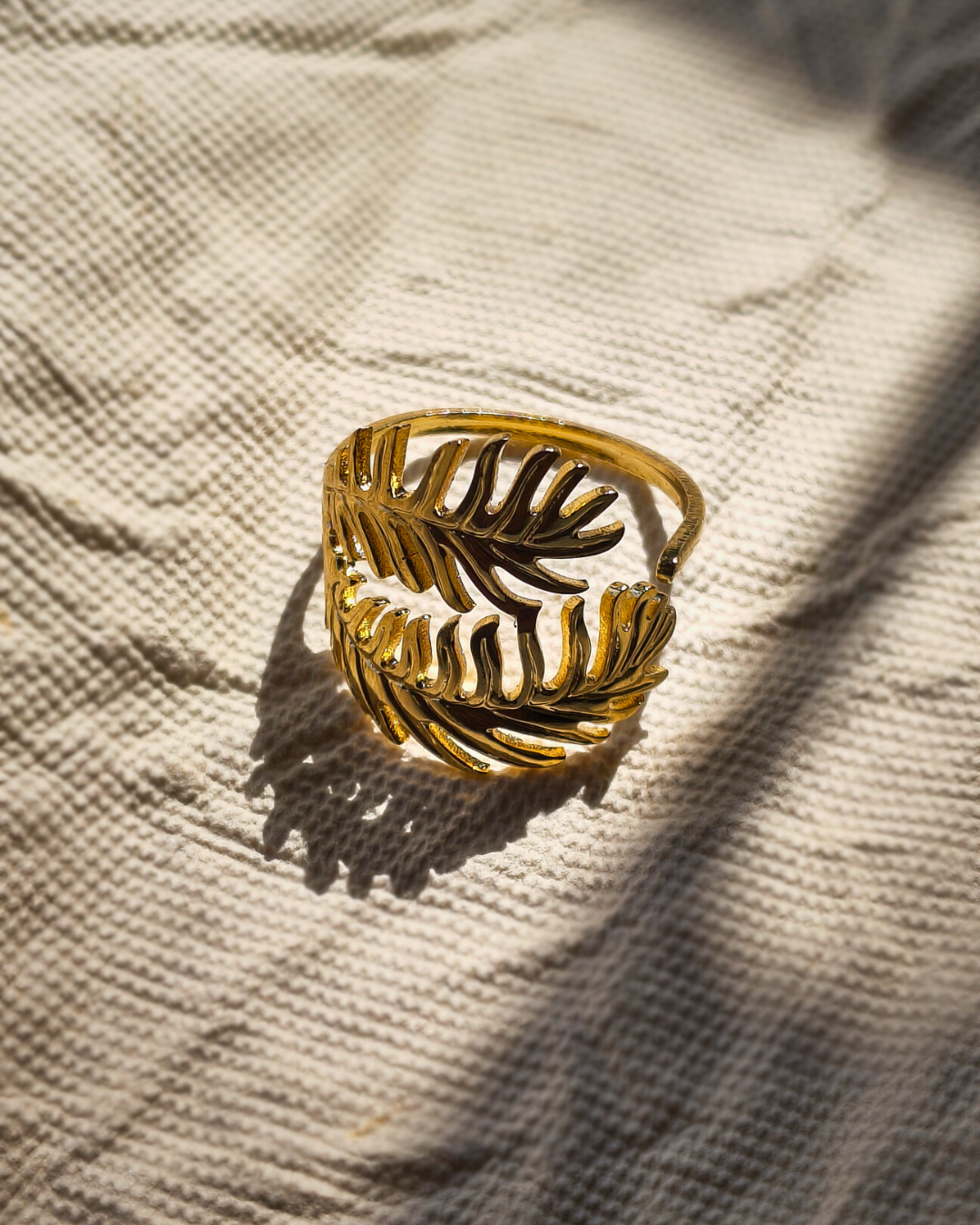 Adjustable gold fern ring with botanical leaf design on textured fabric background.