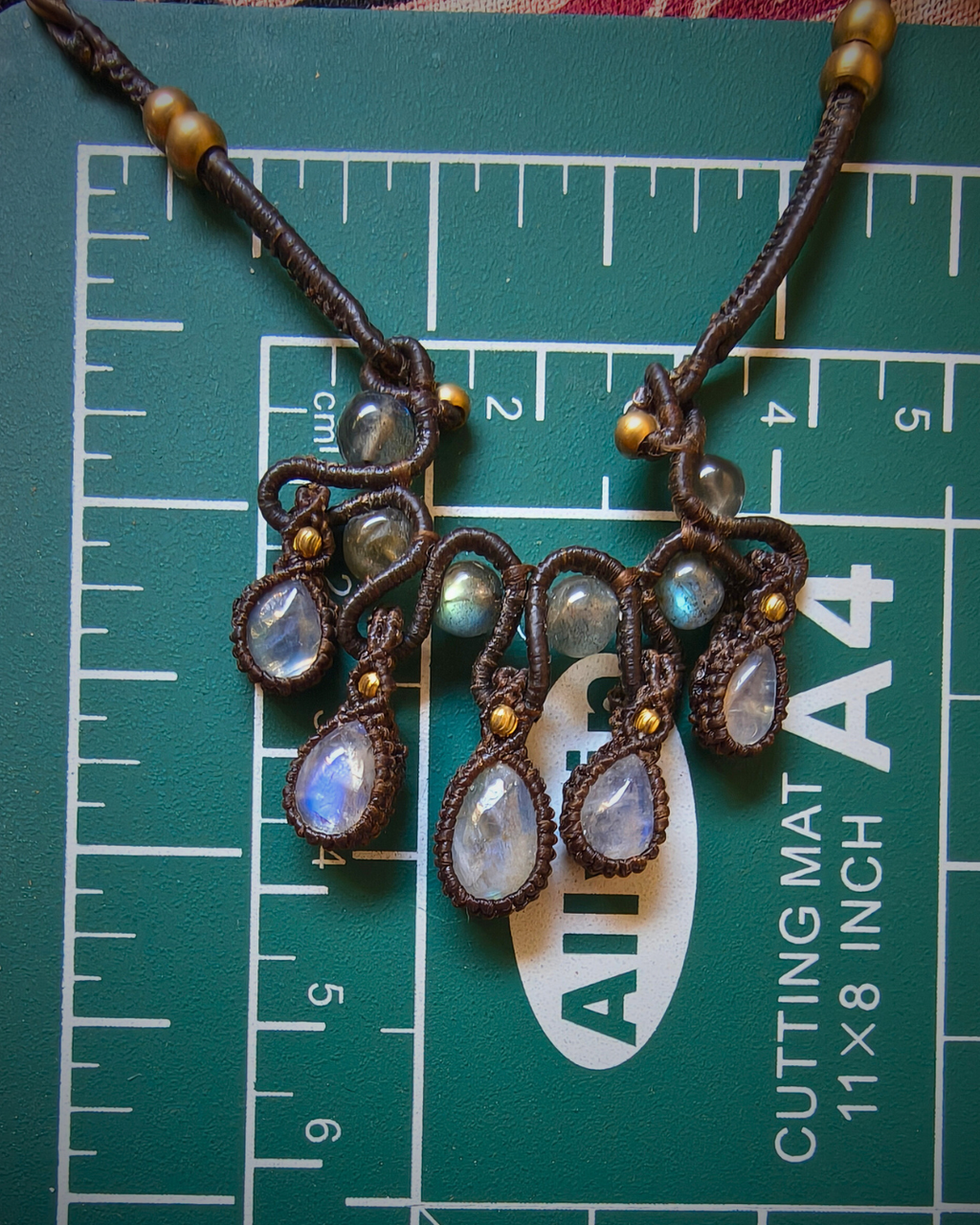 Adjustable boho macrame necklace with moonstone drops and brass beads on measurement mat for actual size