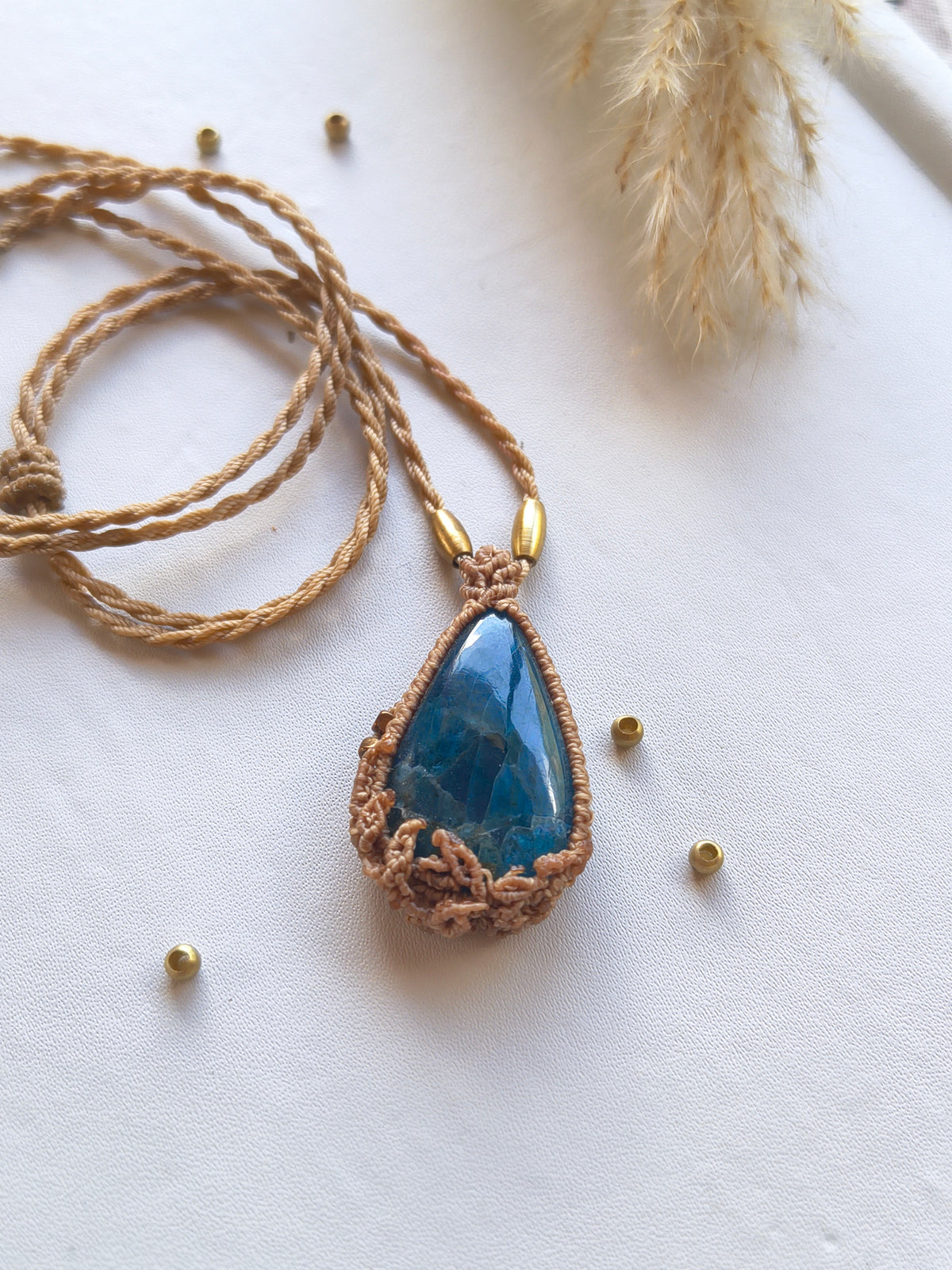 Close-up of deep blue apatite gemstone cabochon set with detailed macrame threads handmade in leaf design 