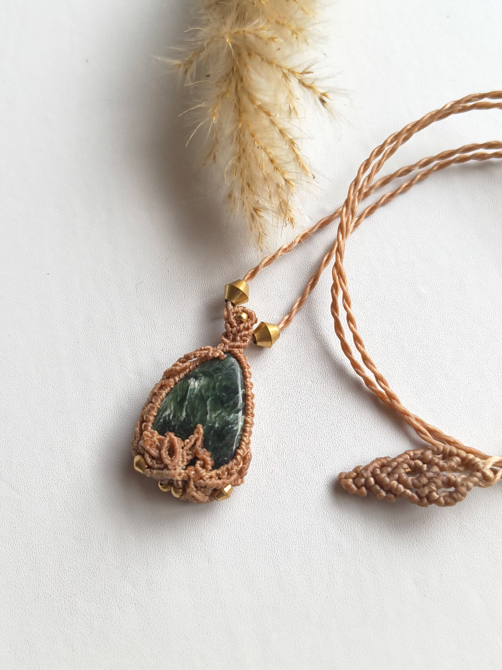 Close-up of seraphinite showing green feathered mineral patterning and dried leaf macrame design 
