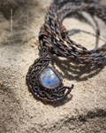 Necklace with a moonstone pendant half moon design on a sandy surface