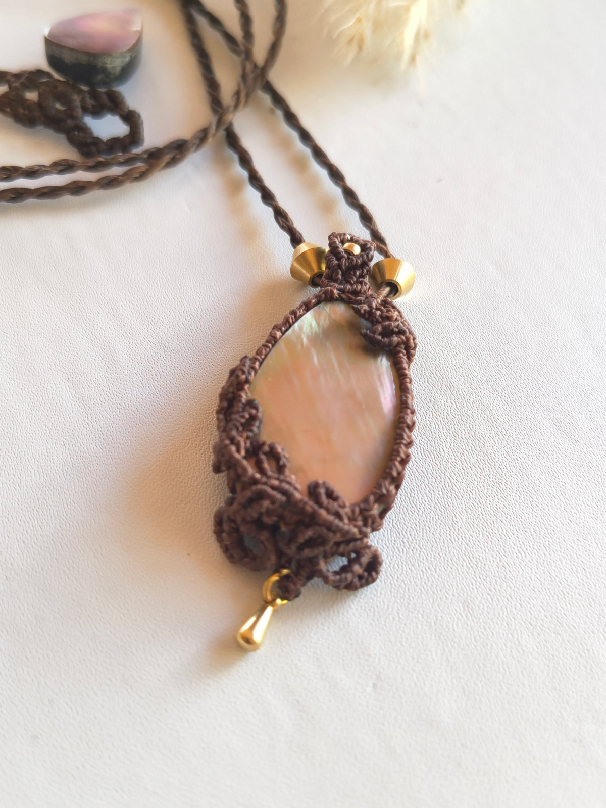 Hand-knotted macramé detail around mother of pearl pendant with brass beads and dangles