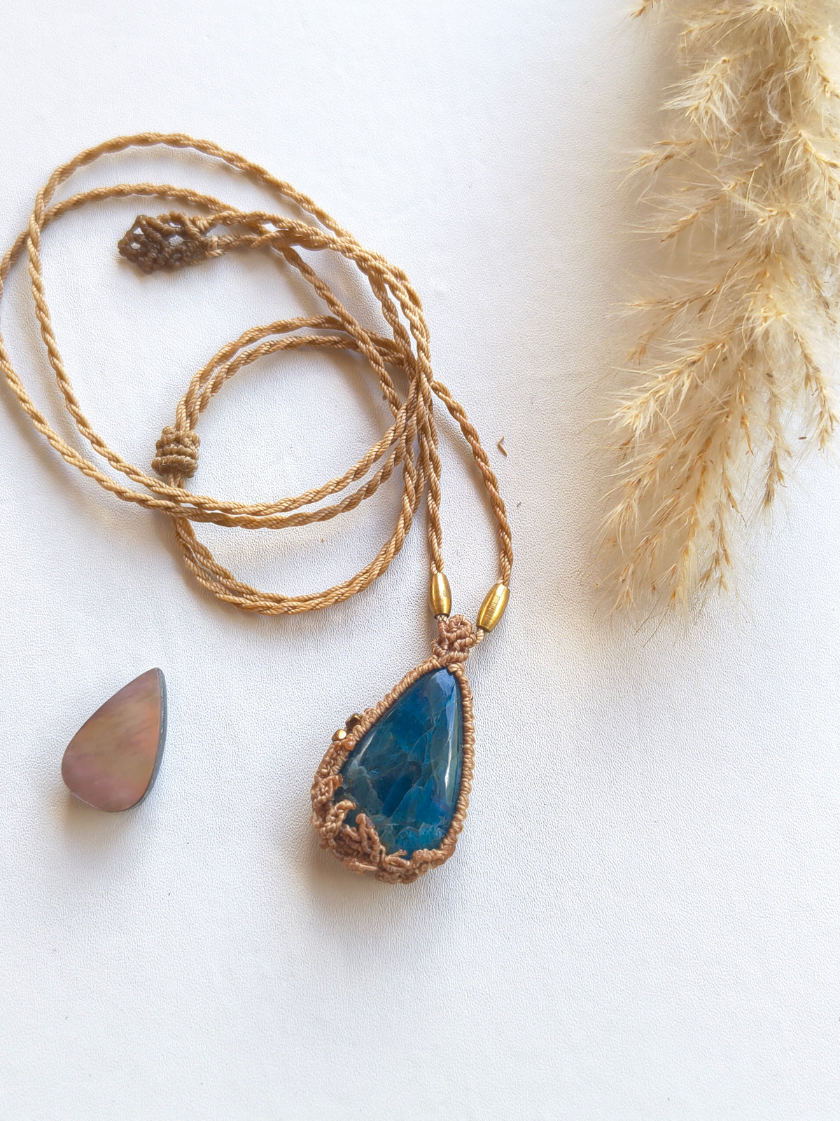Hand-knotted macramé leaves detail around blue apatite pendant top view layout flat on white background 