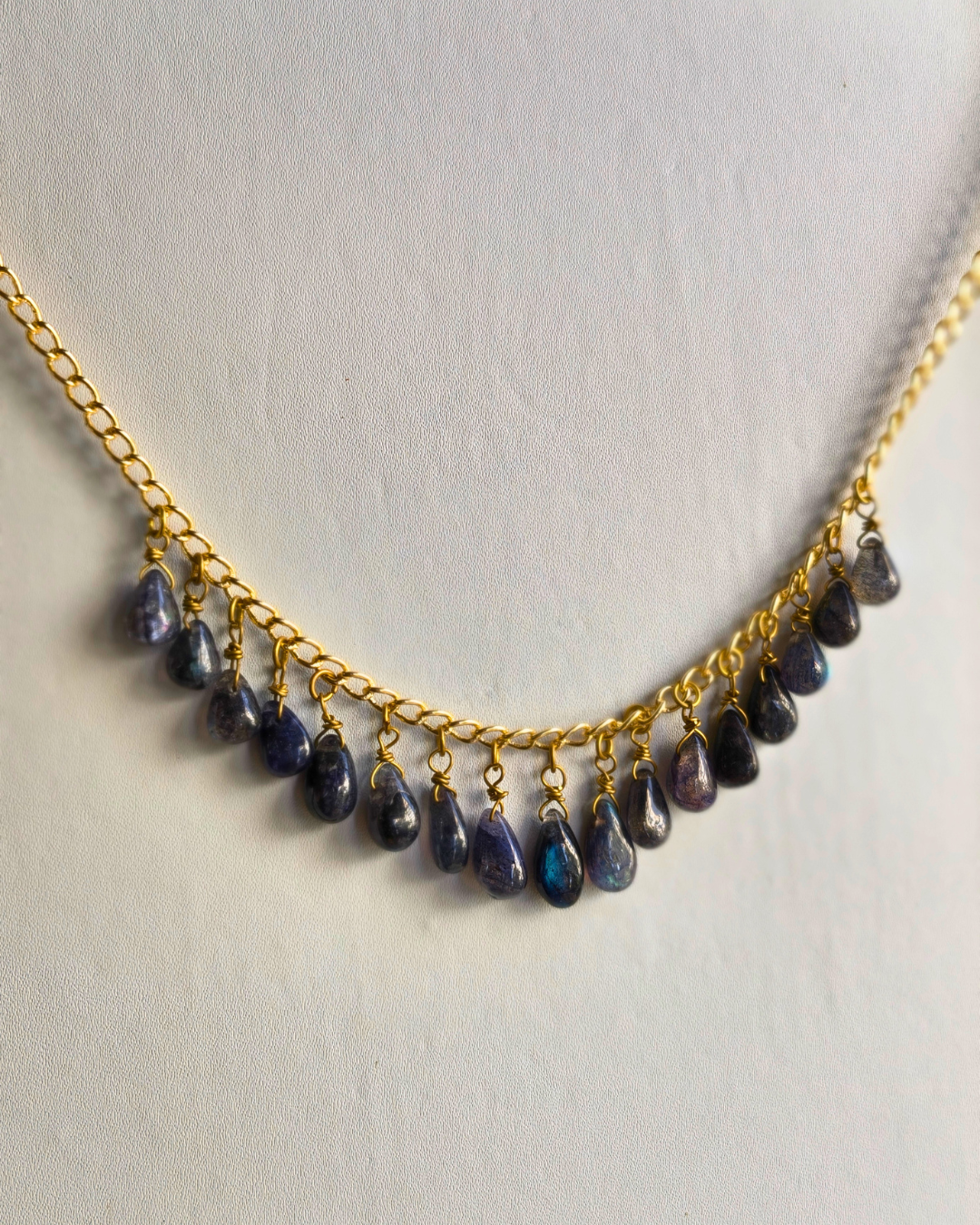 Necklace with gold chain and teardrop-shaped blue stones on a light gray background