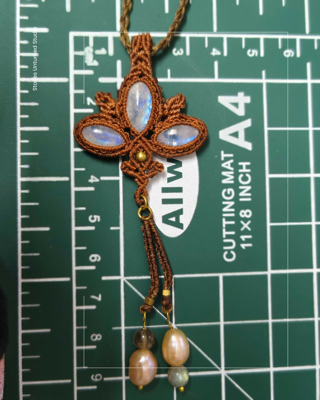 Close-up of lotus shaped macrame pendant featuring three rainbow moonstones on measuring mat to show true size 