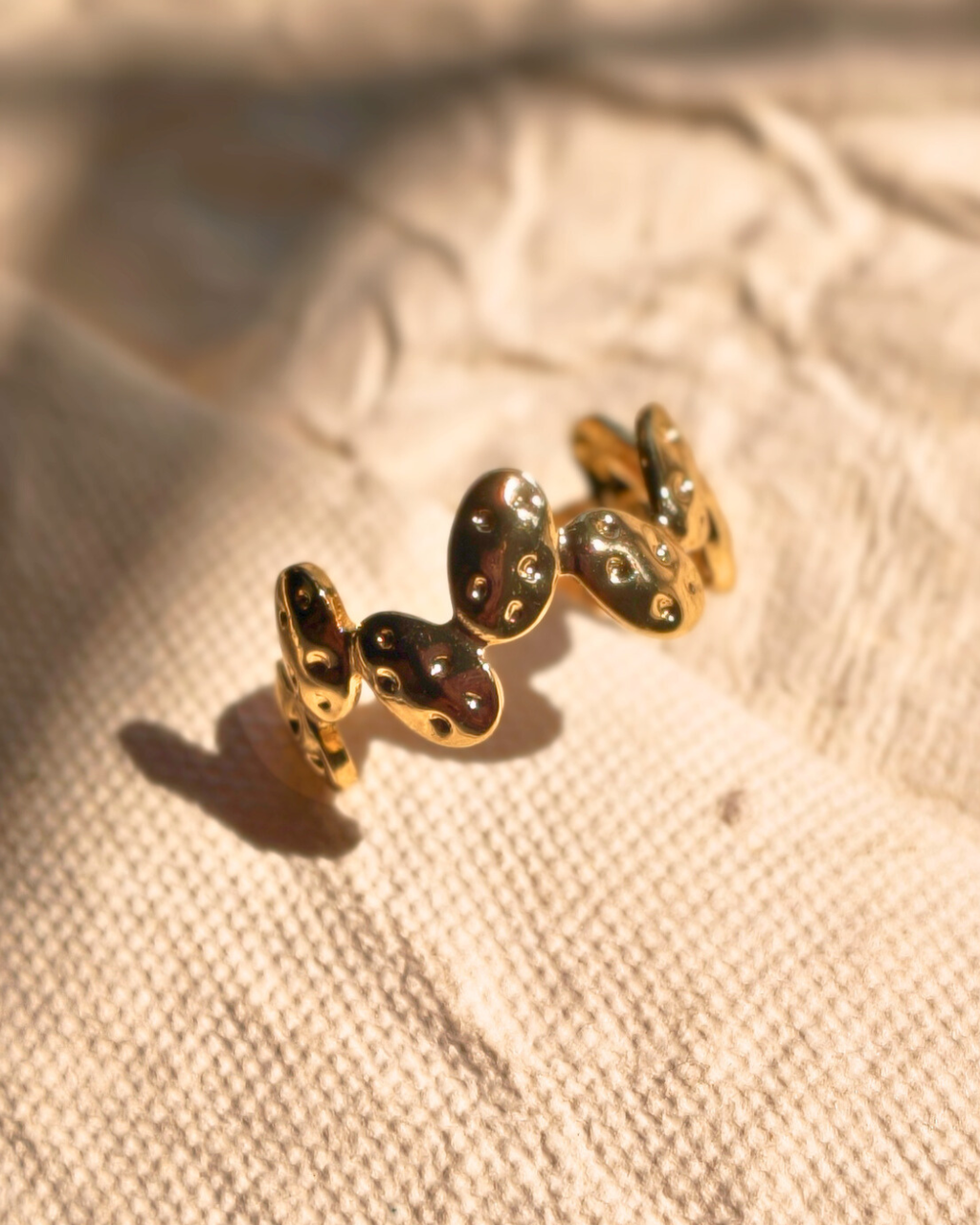 Minimalist gold plated pebble ring on textured fabric background