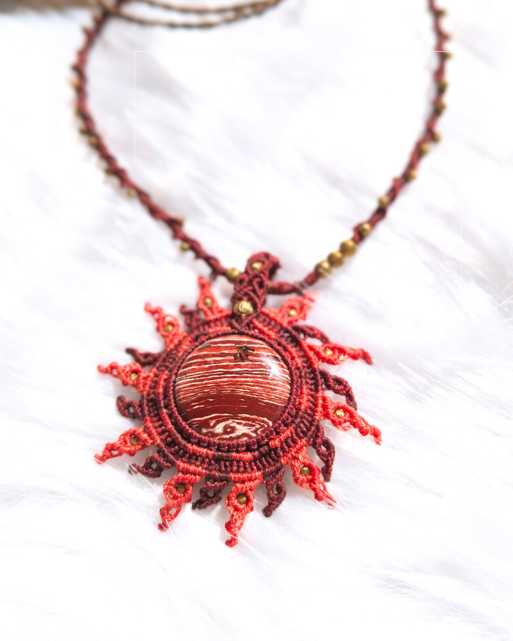 Rainbow jasper sunset pendant showing red and white stone pattern with woven sun rays