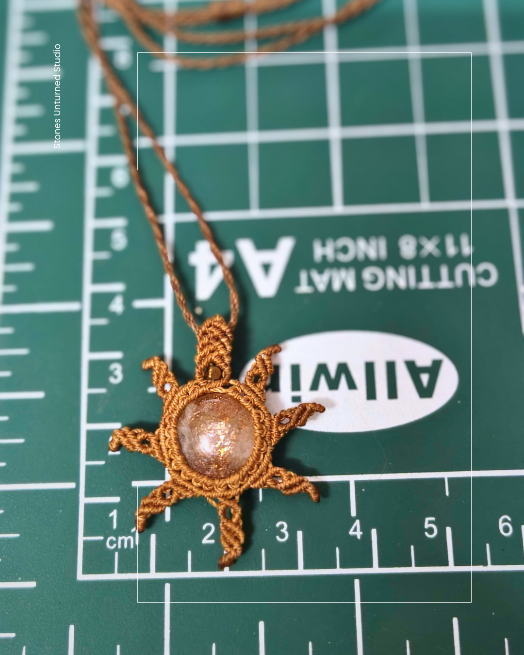 Sun-shaped macrame handmade  gemstone pendant on a chain on a cutting mat with measurements