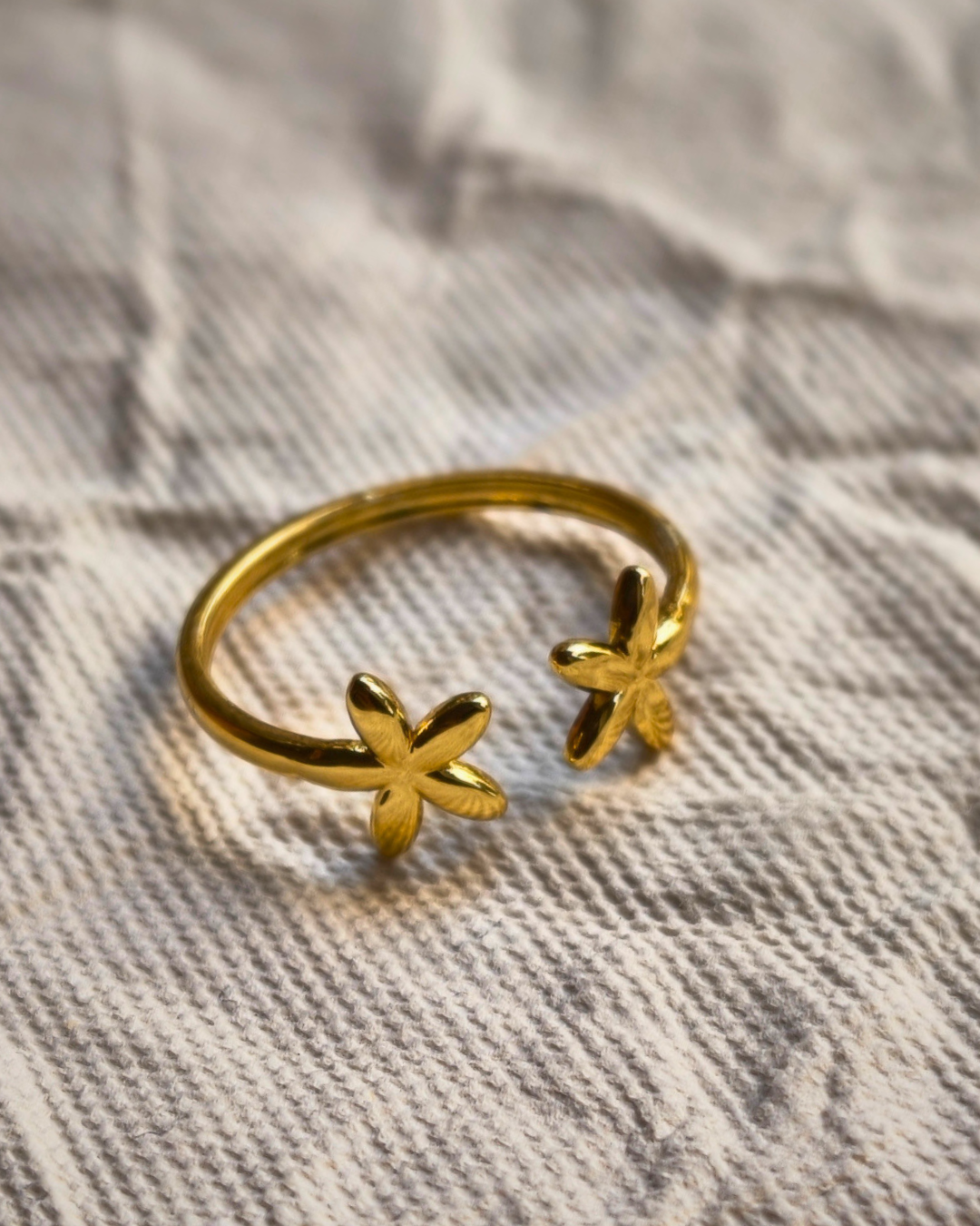 Minimalist gold flower ring on textured fabric background.