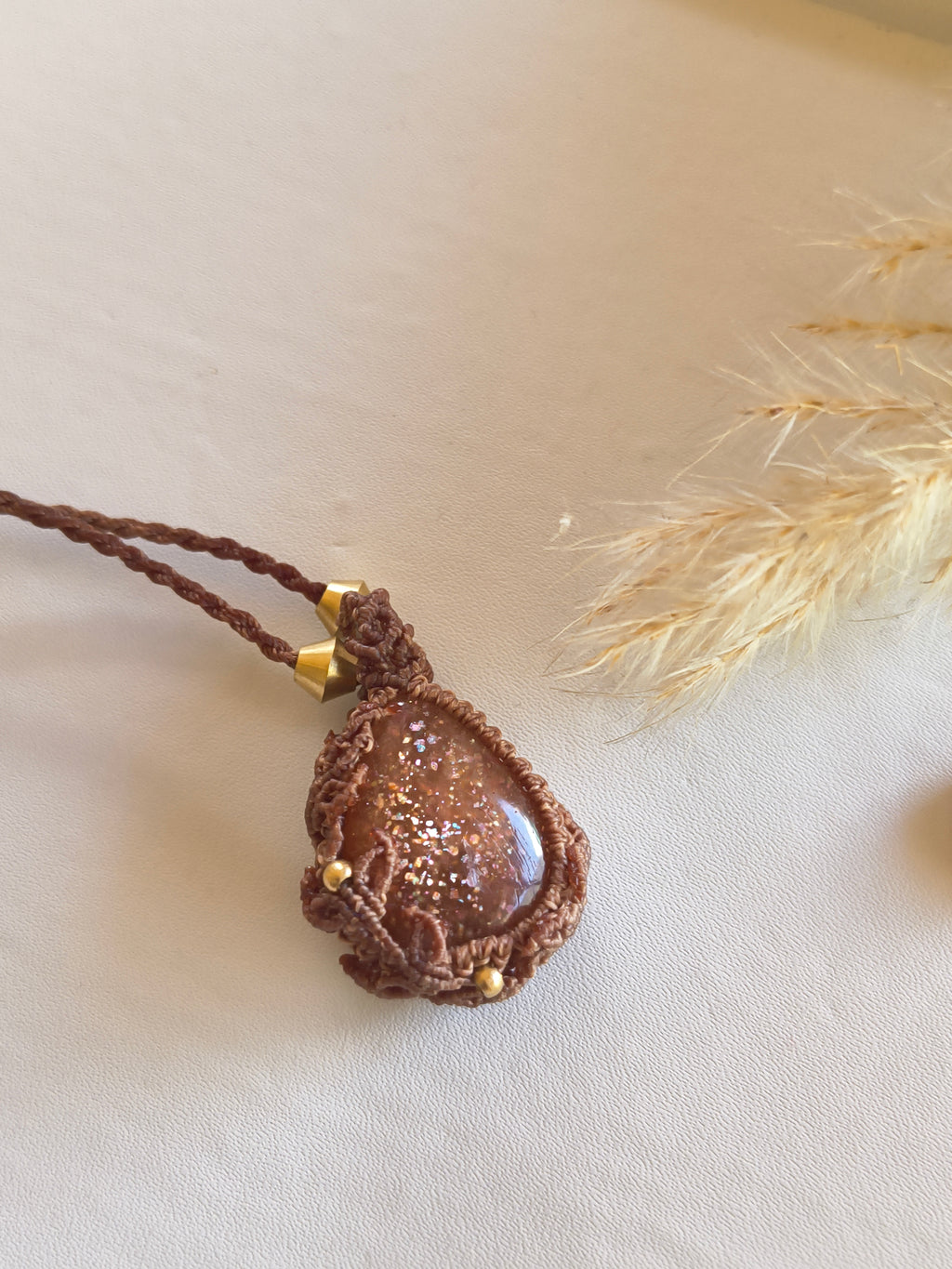 A handmade macrame pendant necklace in brown cord with a high quality teardrop-shaped sunstone with flashes accented with small gold beads. 
